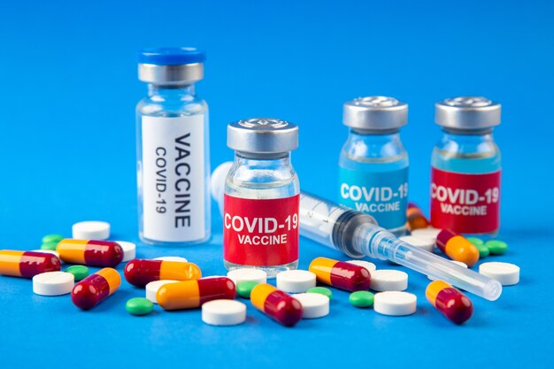 Vista ravvicinata di COVID- vaccini in fiale mediche pillole capsule siringa monouso su sfondo blu scuro e morbido