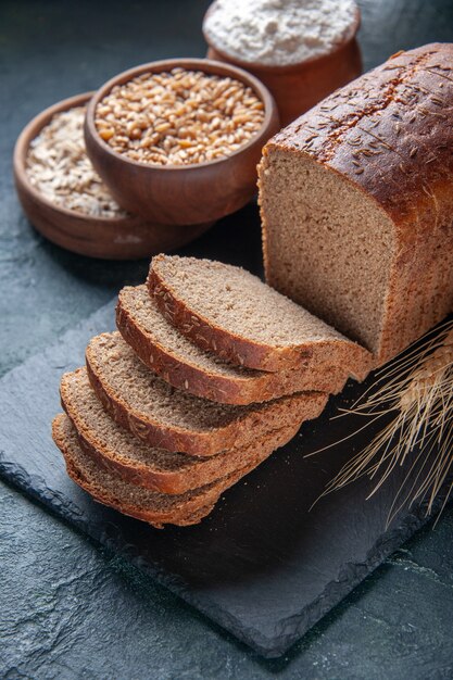 Vista ravvicinata di fette di pane nero farina di farina d'avena grano saraceno su tavola di colore scuro su sfondo blu in difficoltà