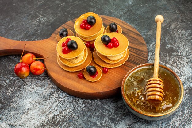 Vista ravvicinata di frittelle di frutta sul tagliere di legno miele in una ciotola bianca su grigio