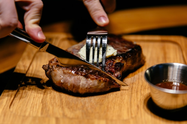 Vista ravvicinata di gustosa bistecca con salsa. Le mani di un uomo iniziano a tagliare una fetta.