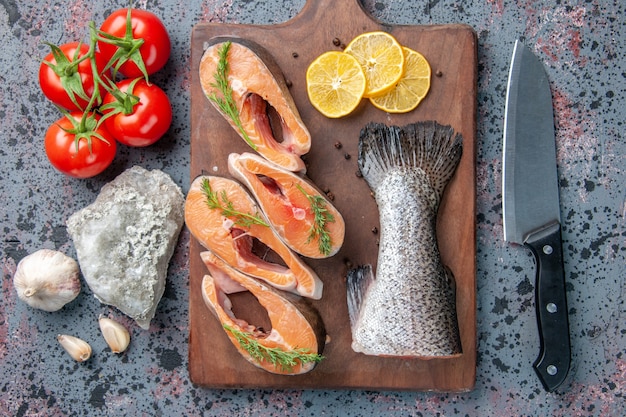 Vista ravvicinata di pesce crudo fette di limone verdi pepe sul tagliere di legno e coltello per alimenti sulla tabella colori blu nero