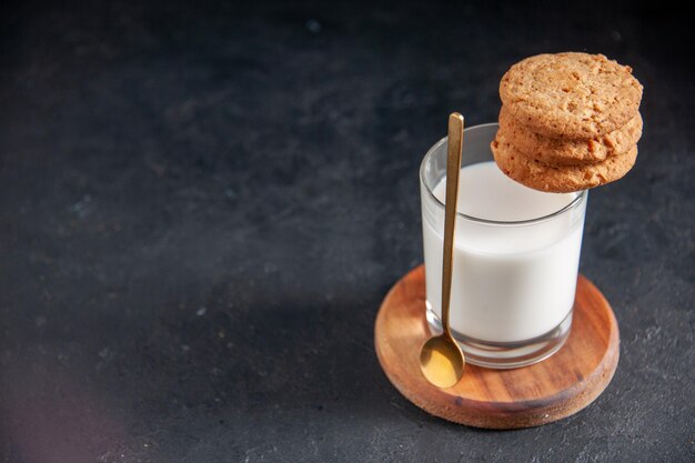 Vista ravvicinata di un bicchiere di biscotti al latte e cucchiaio d'oro sul lato sinistro su un piccolo vassoio di legno marrone su sfondo nero