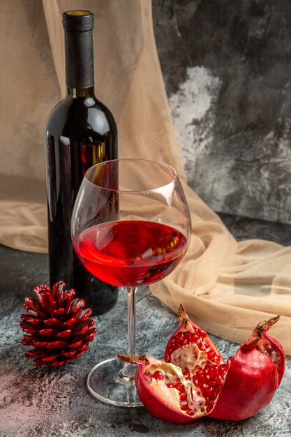 Vista ravvicinata di un bicchiere e una bottiglia con un delizioso vino rosso secco e un cono di conifere di melograno aperto su sfondo di ghiaccio