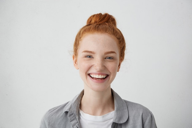 Vista ravvicinata di una bella donna con nodo di capelli rossi, occhi blu affascinanti, lentiggini e sorriso gentile con un'espressione deliziosa