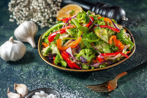 Vista ravvicinata di una deliziosa insalata di verdure con vari ingredienti aglio forchetta sale martello nero su sfondo scuro