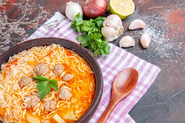 Vista ravvicinata di una deliziosa zuppa di pollo con noodles verdi e cucchiaio su un asciugamano spogliato rosa bottiglia di olio aglio limone su sfondo scuro