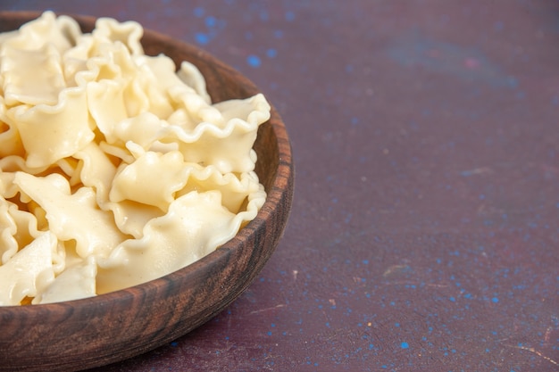 Vista ravvicinata frontale a fette di pasta cruda all'interno del piatto marrone su uno spazio scuro