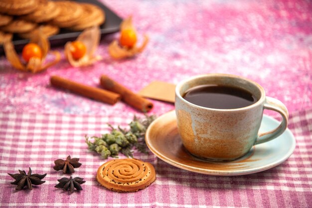 Vista ravvicinata frontale biscotti dolci deliziosi piccoli biscotti con una tazza di tè sulla scrivania rosa chiaro.