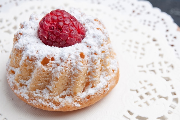 Vista ravvicinata frontale deliziosa torta con crema e lampone rosso sul biscotto alla frutta torta di tessuto bianco