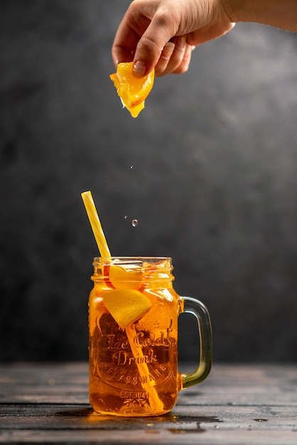 Vista ravvicinata frontale di un delizioso succo naturale fresco in una mano di vetro che mette lime arancioni con tubo in esso su sfondo nero