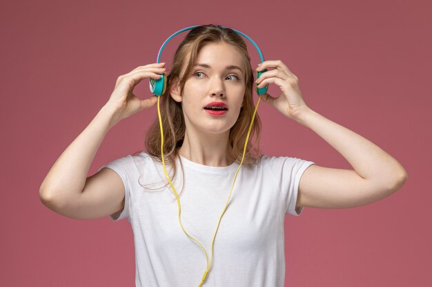 Vista ravvicinata frontale giovane femmina attraente ascoltando musica tramite auricolari sul muro rosa modello colore femmina giovane