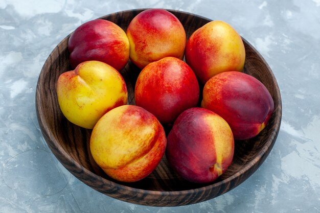 Vista ravvicinata frontale pesche fresche frutta pastosa e gustosa all'interno del piatto marrone sullo scrittorio bianco-chiaro