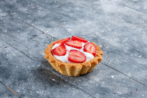 Vista ravvicinata frontale piccola torta cremosa con fragole a fette su grigio, torta di frutti di bosco dolce cuocere