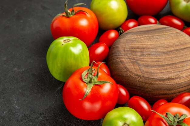 Vista ravvicinata inferiore pomodori rossi e verdi ciliegia intorno a un piatto di legno su sfondo scuro