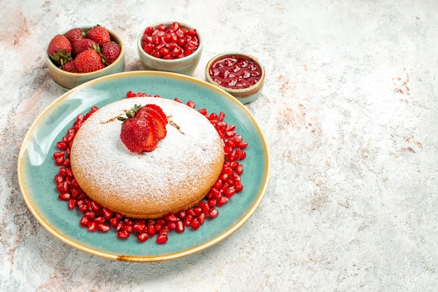 Vista ravvicinata laterale appetitosa torta di fragole e melograno e ciotole di frutti di bosco sul tavolo