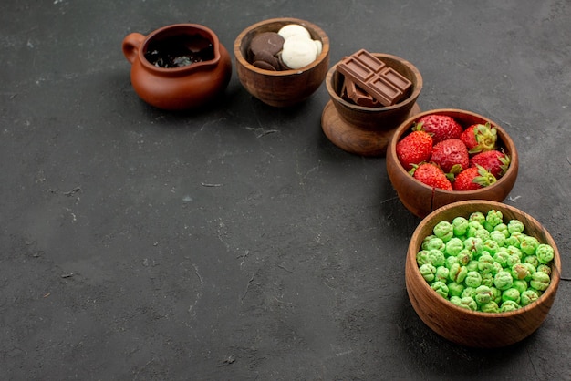 Vista ravvicinata laterale ciotole di caramelle cinque ciotole marroni di cioccolato caramelle verdi fragole e crema al cioccolato sul lato destro del tavolo scuro