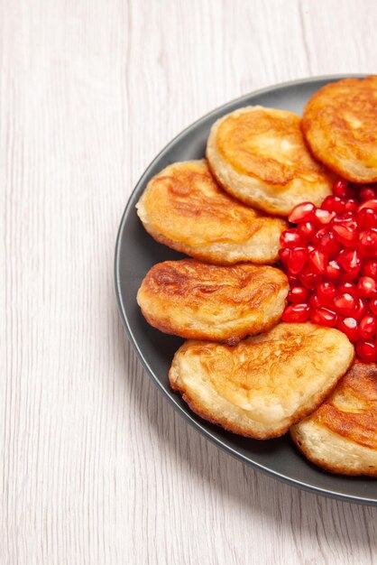 Vista ravvicinata laterale frittelle al melograno e frittelle appetitose sulla banda nera sul tavolo bianco