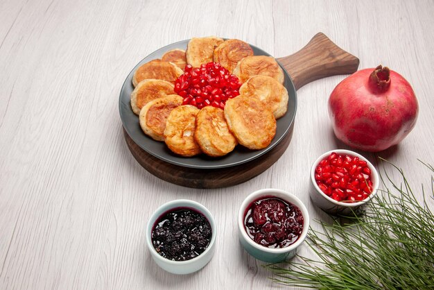 Vista ravvicinata laterale frittelle e ciotole di marmellata di semi di melograno e marmellata e piatto di frittelle appetitose e melograno sul tagliere di legno sul tavolo