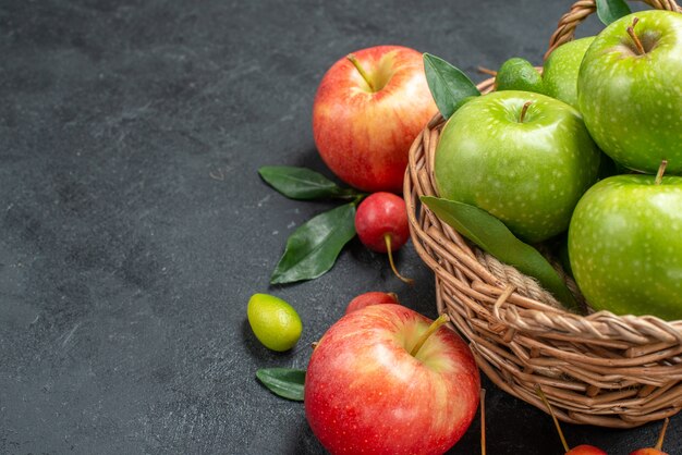 Vista ravvicinata laterale frutta ciliegie mele cesto di mele verdi con foglie