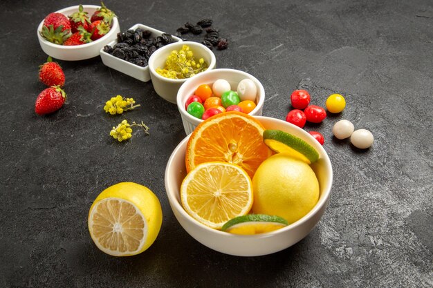Vista ravvicinata laterale frutta e bacche appetitose ciotole di fragole fette di lime limoni arance e caramelle sul tavolo