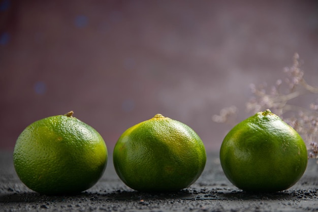 Vista ravvicinata laterale lime sul tavolo scuro tre lime verde-giallo accanto ai rami sul tavolo grigio e su sfondo viola