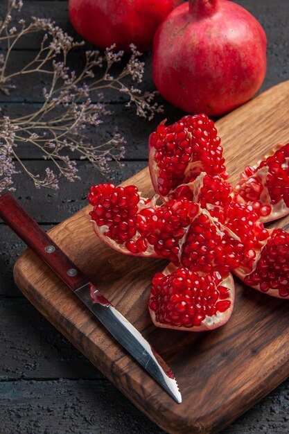 Vista ravvicinata laterale melograno pilled e rami melograno pilled sul bordo della cucina accanto ai rami degli alberi coltello e due melograni su sfondo scuro