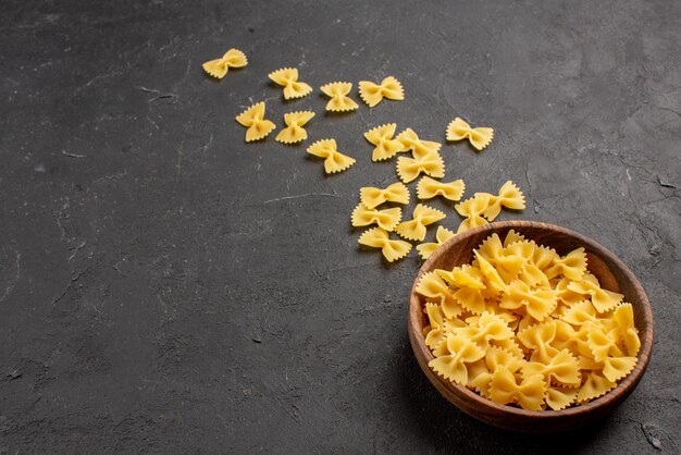 Vista ravvicinata laterale pasta in ciotola di legno sul lato destro del tavolo scuro