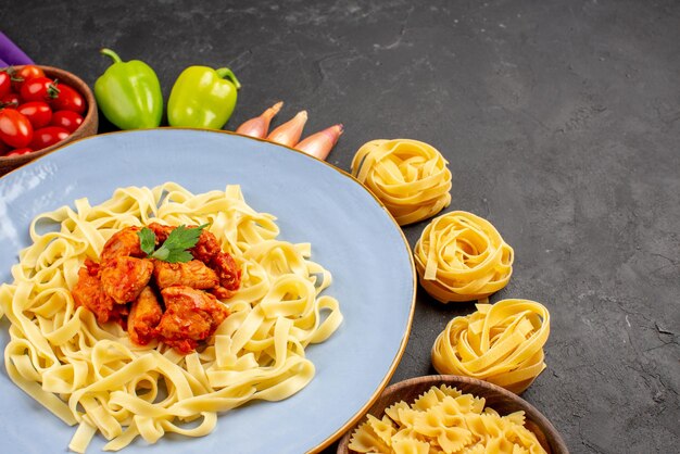 Vista ravvicinata laterale piatto di cibo piatto di pasta con carne e sugo di cipolla pepe palla ciotola di pomodori sulla tovaglia