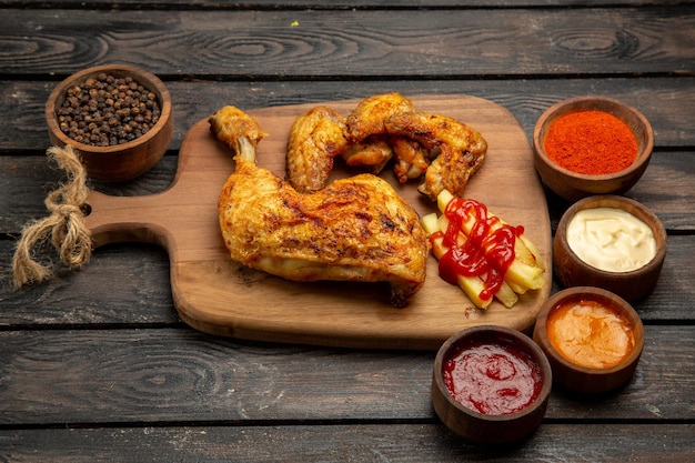 Vista ravvicinata laterale pollo fastfood e patatine fritte sul bordo della cucina accanto al ketchup pepe nero salse e spezie sul tavolo
