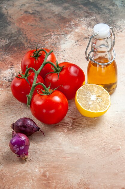 Vista ravvicinata laterale pomodori bottiglia di olio pomodori cipolle limone sul tavolo