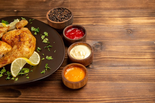 Vista ravvicinata laterale salse e ciotole di pollo di tre tipi di salse e pepe nero accanto al piatto di pollo con erbe e limone sul lato sinistro del tavolo