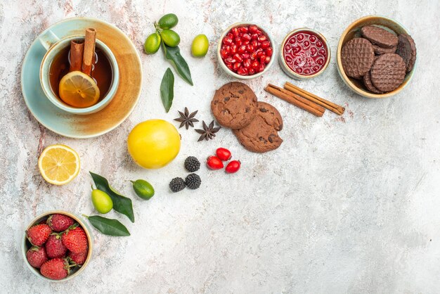 Vista ravvicinata laterale tè con biscotti ai frutti di bosco la tazza di tè con fragole al limone agrumi sul tavolo