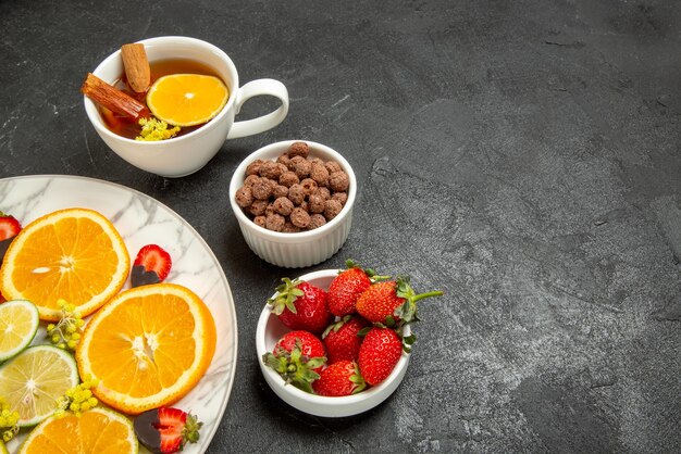 Vista ravvicinata laterale tè e frutta piatto di pezzi di limone arancia fragole ricoperte di cioccolato una tazza di tè e ciotole di nocciole e fragole sul lato destro del tavolo