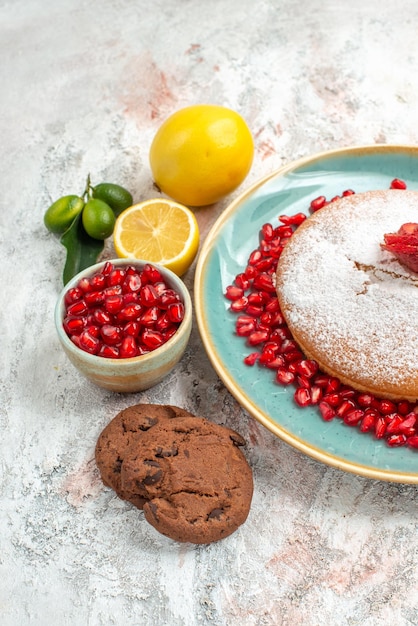 Vista ravvicinata laterale torta di fragole piatto blu di torta con fragole e melograno accanto alla ciotola di limone di melograno e biscotti sul piatto