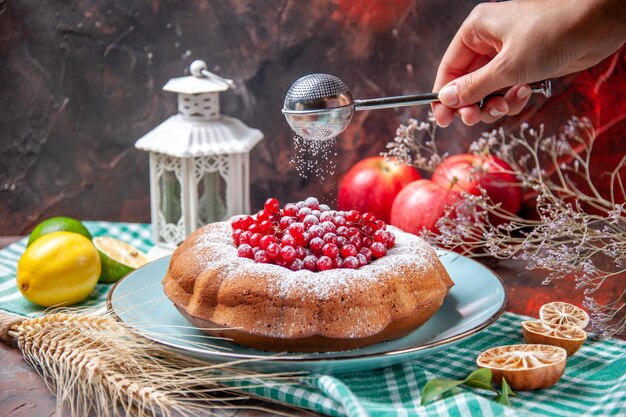 Vista ravvicinata laterale una torta una torta appetitosa con frutti di bosco limoni tre mele cucchiaio in mano