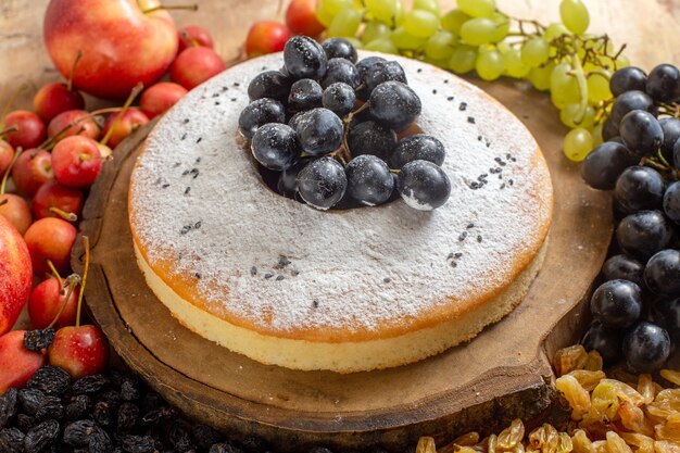 Vista ravvicinata laterale una torta una torta appetitosa sulla tavola di legno uva uva passa mele ciliegia