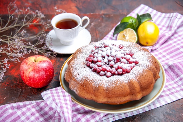 Vista ravvicinata laterale una torta una torta con frutti di bosco agrumi sulla tovaglia una tazza di tè