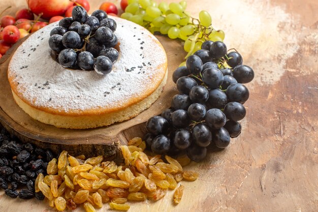 Vista ravvicinata laterale una torta una torta con l'uva sulla tavola di legno uva passa ciliegia mele uva