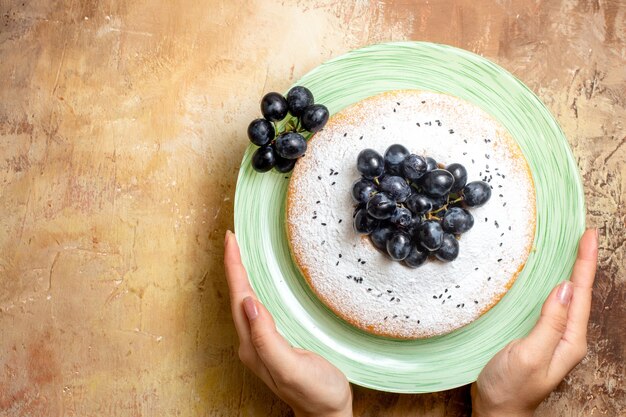 Vista ravvicinata superiore un piatto verde della torta di una torta appetitosa con l'uva nelle mani