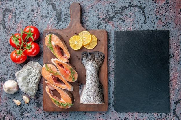 Vista sopra di pesce crudo fette di limone verdi pepe sul tagliere di legno e posate di verdure impostato sul vassoio di colore scuro su blu nero colori tabella