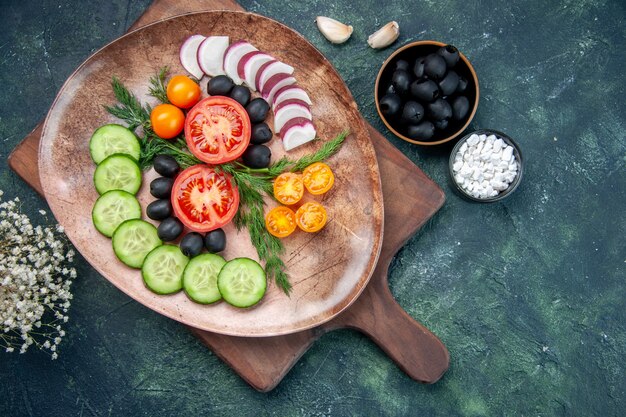 Vista sopra di verdure fresche tritate in una piastra marrone sul tagliere di legno olive nella ciotola sale garlics fiore su colori misti tabella