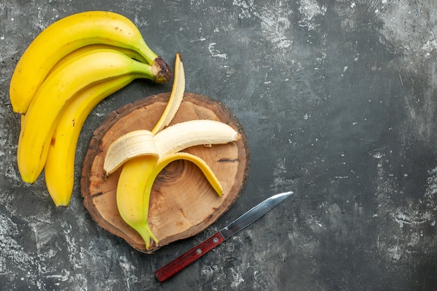 Vista sopra la fonte di nutrizione pacco di banane fresche e sbucciate su tagliere di legno coltello su sfondo grigio