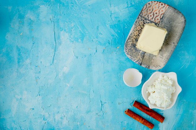 Vista superiore degli alimenti come cannella della ricotta del burro con il guscio d'uovo su fondo blu con lo spazio della copia