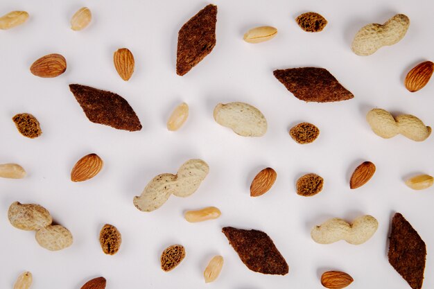 Vista superiore degli spuntini arachidi della mandorla con buccia e senza buccia e cracker piccanti su bianco