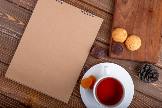 Vista superiore dei biscotti dello sketchbook e una tazza di tè con i bastoncini di cannella su fondo di legno
