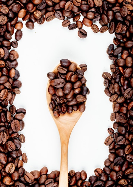 Vista superiore dei chicchi di caffè in un cucchiaio di legno su fondo bianco