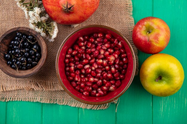 Vista superiore dei frutti in ciotole con melograno fiore su tela di sacco e mele sulla superficie verde