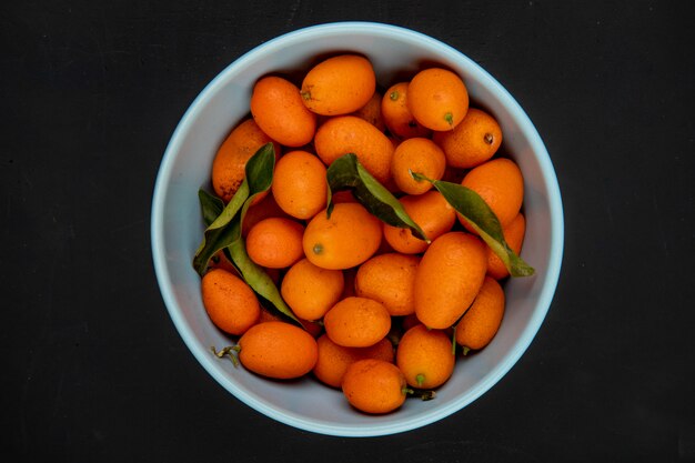 Vista superiore dei kumquat maturi freschi in una ciotola blu sul nero