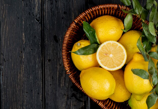 Vista superiore dei limoni maturi freschi in un cestino di vimini sul nero con lo spazio della copia