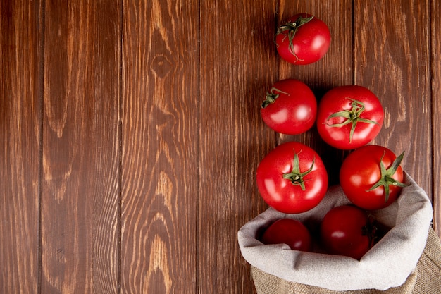 Vista superiore dei pomodori che si rovesciano dal sacco dalla destra e dal legno con lo spazio della copia